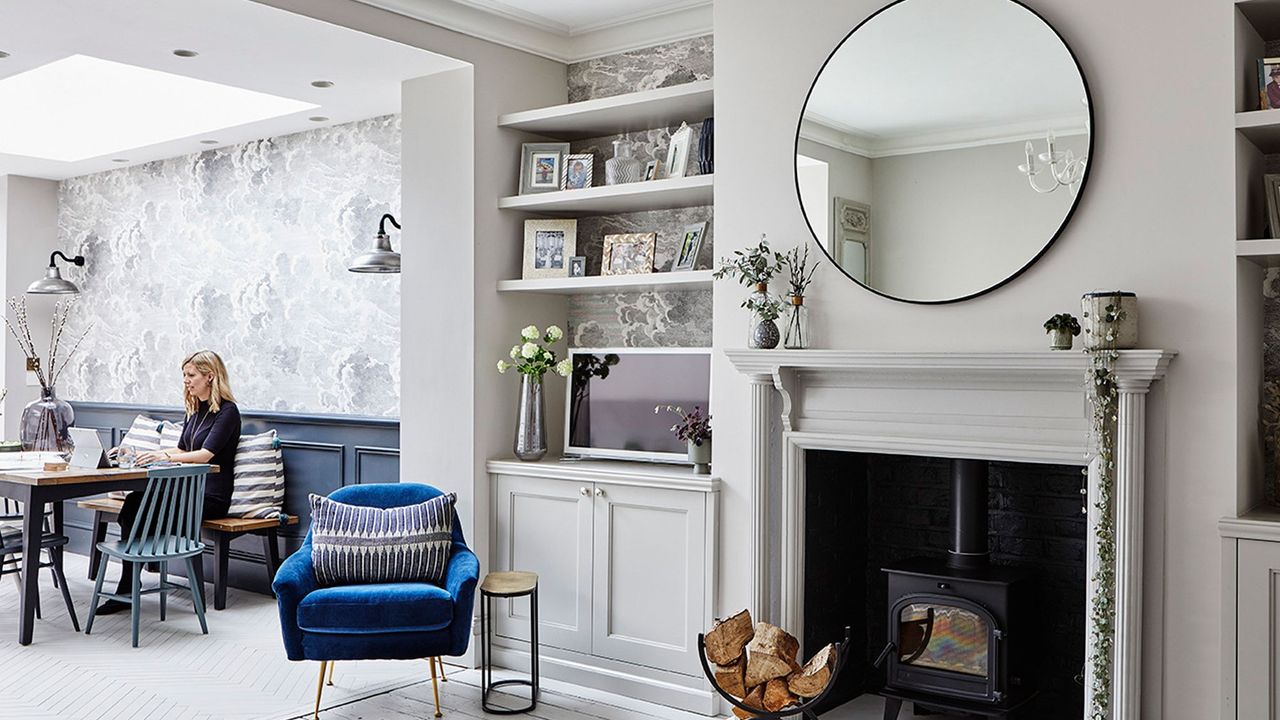 A grey living and dining room with a wood burning stove, patterned grey wallpaper and a dining table with blue and grey chairs