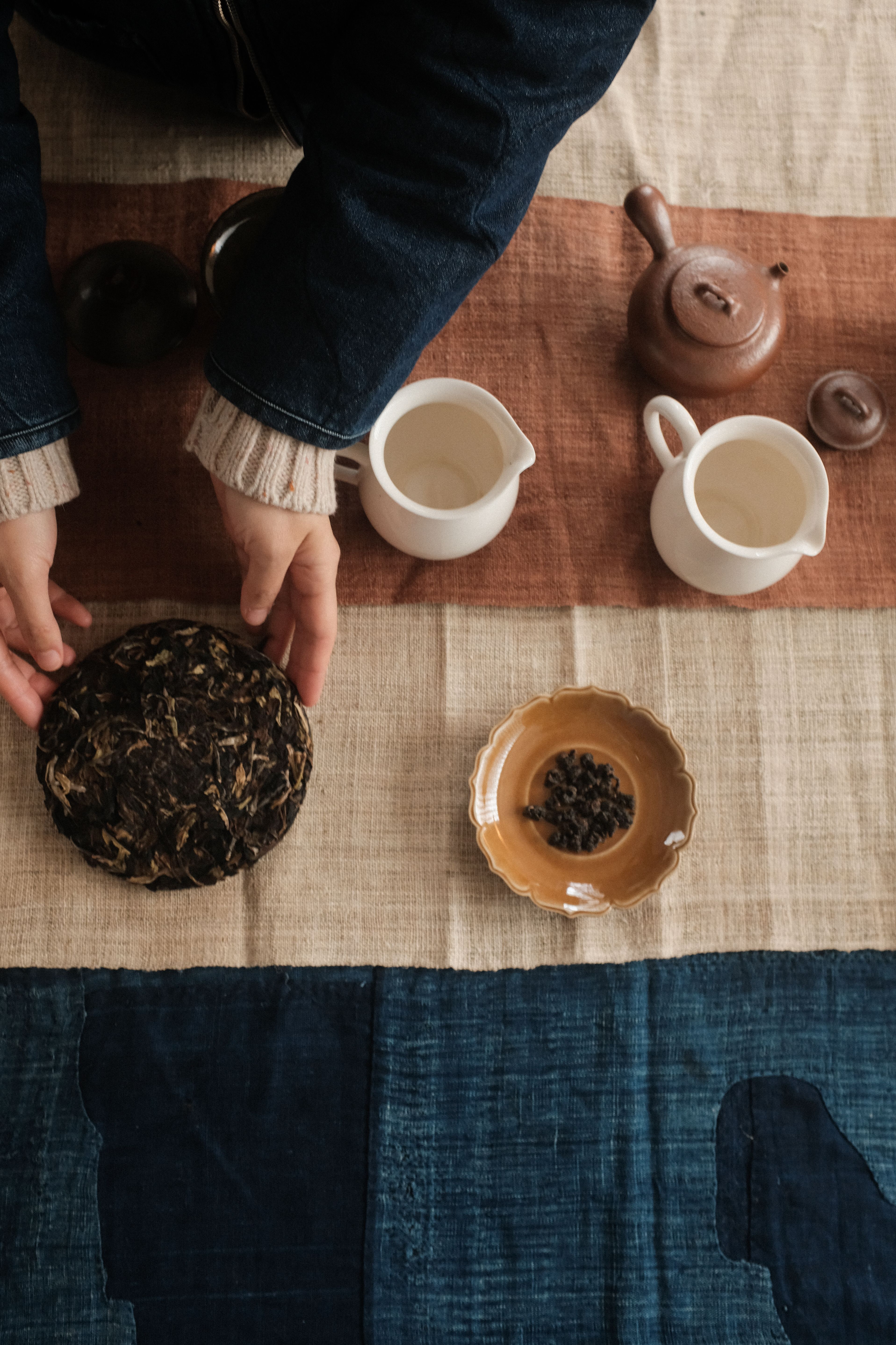A traditional Vietnamese tea time setup, with ceramic mugs, slices of cakes, and a leaf blend all positioned atop a Vietnamese flag in a naturally lit gallery.