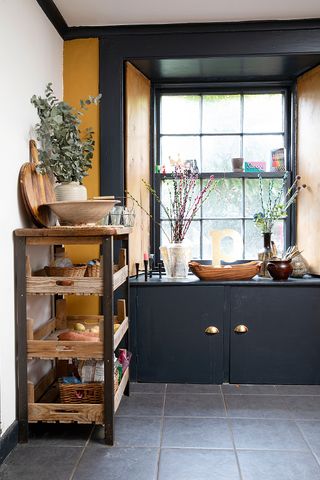 Black kitchen storage cupboards under a window and freestanding shelving