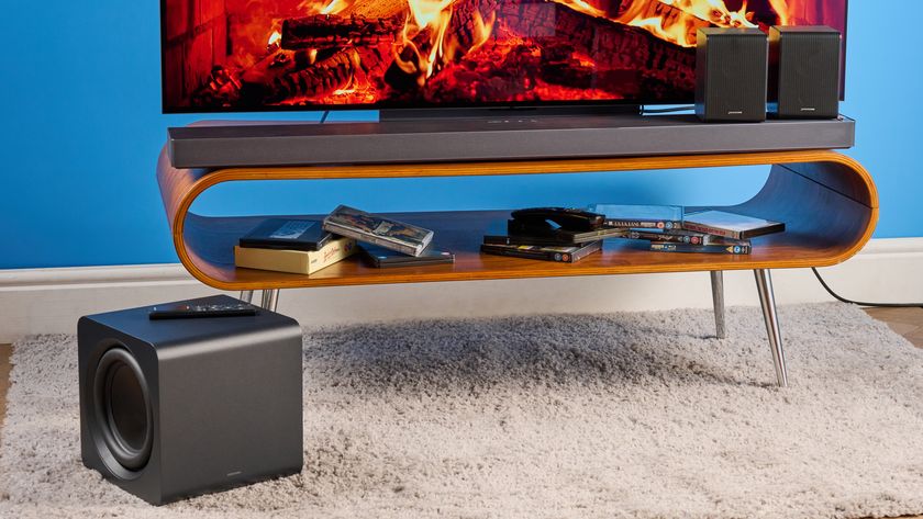 the samsung qs750f soundbar with two rear surround speakers and subwoofer photographed against a blue background and a TV