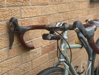 A black bike light attached out front to the handlebars with a small camera on the left and the bike light on the right. It is attached beneath a garmin mount.