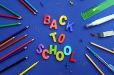 back to school written in different bright letters on a blue background with stationery scattered around