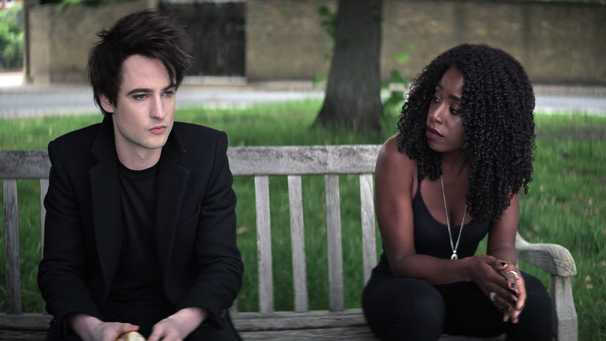 (L to R) Tom Sturridge as Dream, Kirby Howell-Baptiste as Death, on a bench, in The Sandman
