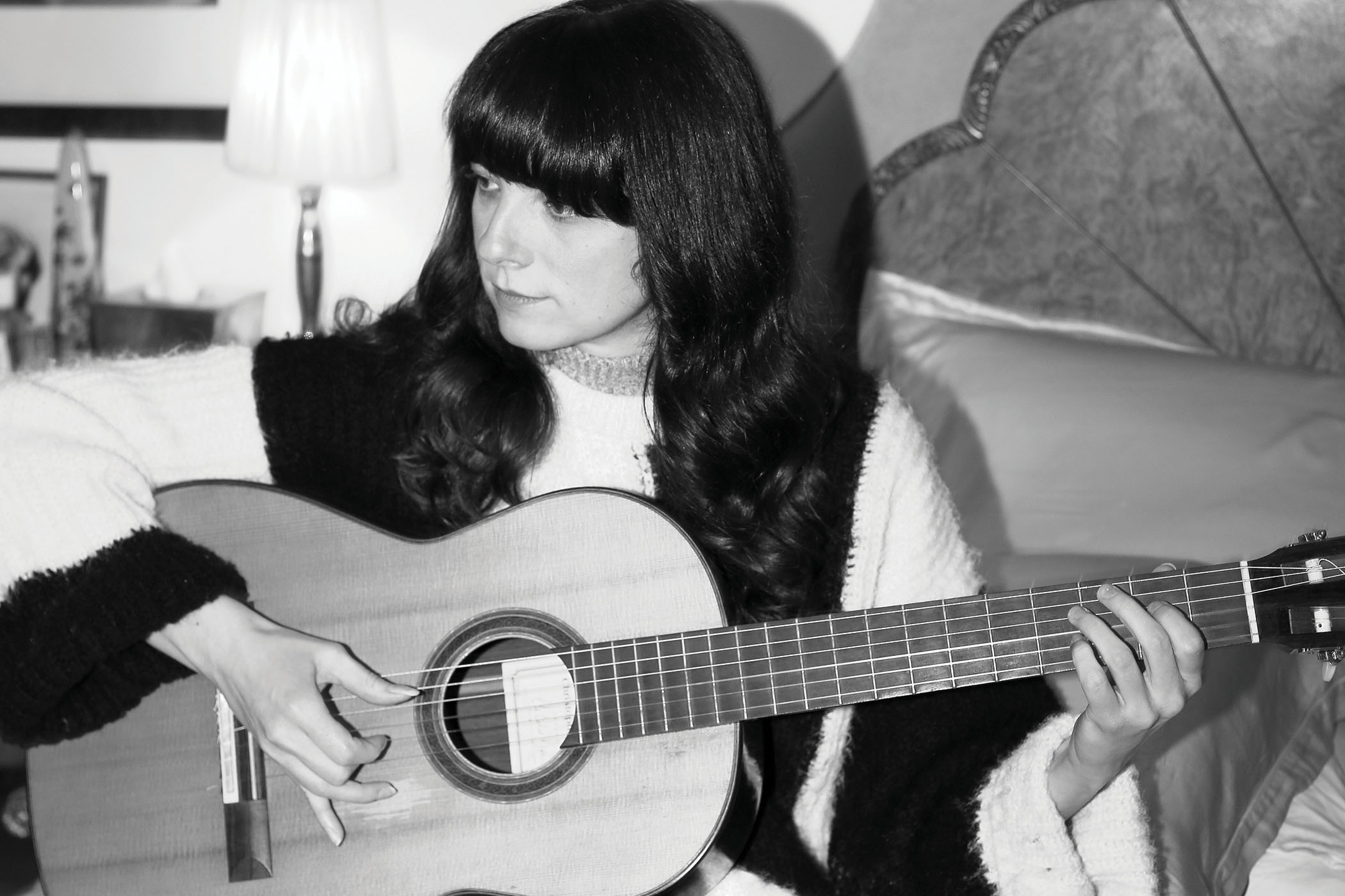 Classical phenom Laura Snowden sits on a bed and plays her guitar