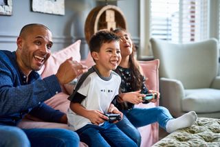 dad playing video games on sofa with children