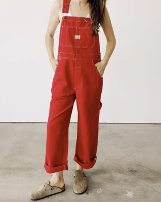 a model wears a pair of red hey gang overalls while standing in front of a plain backdrop