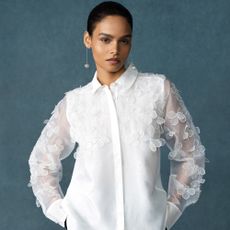 Model wearing a sheer white blouse with flower appliques and long dangly earrings sold at French Connection