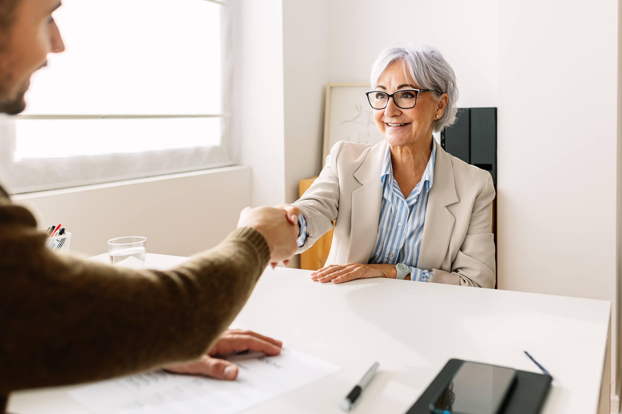 An older woman shakes hands with a young, male recruiter. She is about to be interviewed or has just finished interviewing for a job.