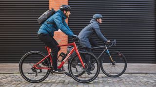 Two cyclists in casual commuting clothing ride on a cobbled street