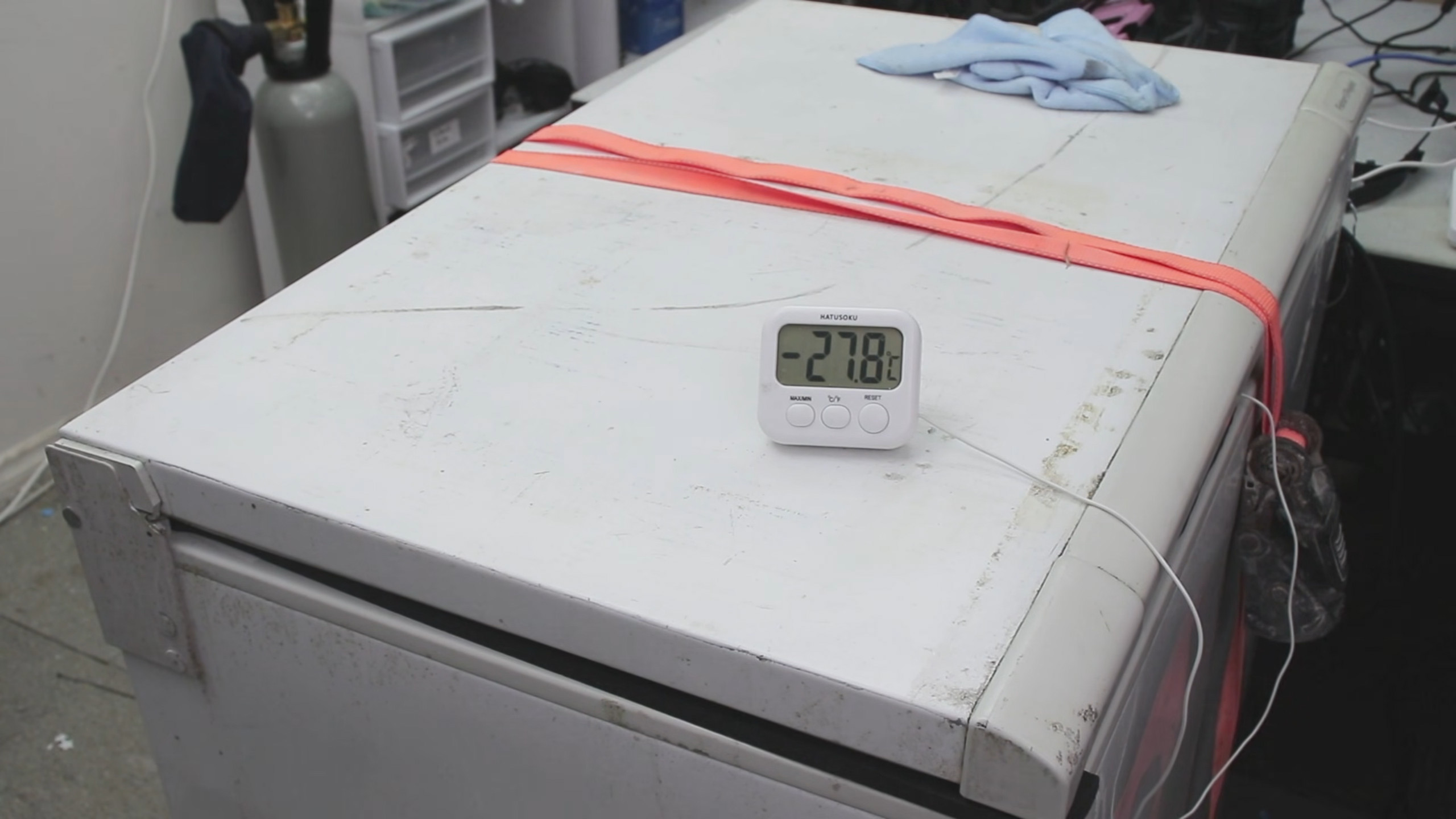 A photo of a freezer held tightly shut by a ratchet strap, with a thermometer showing a temperature of -27.8&amp;#8451;.