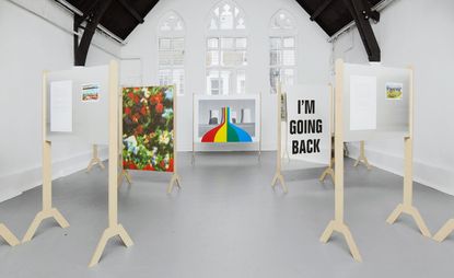 Artwork on wooden stands inside a white room with arched windows and a vaulted ceiling