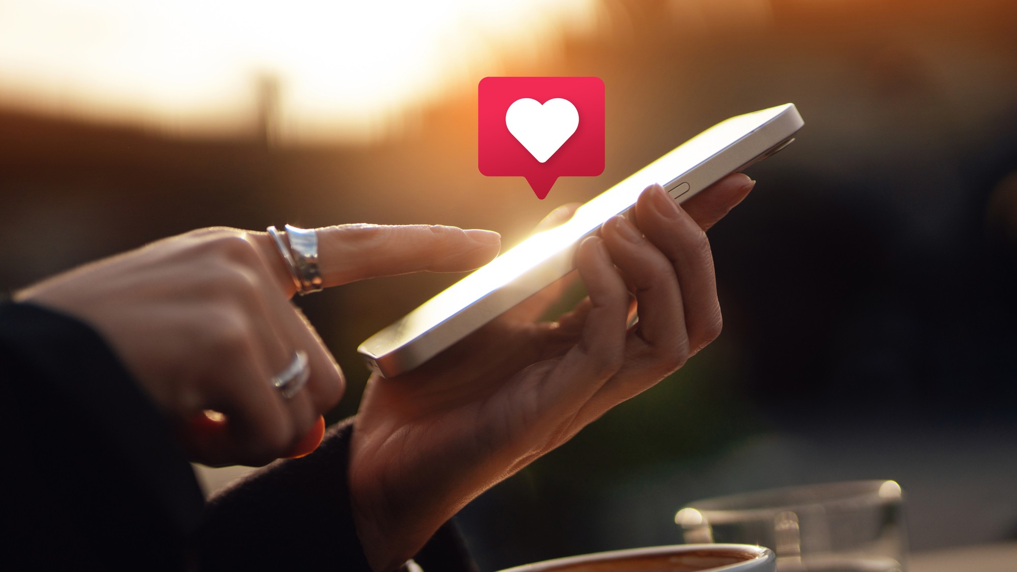 A person holds a cell phone outside and taps the screen. A heart emoji is above the phone.
