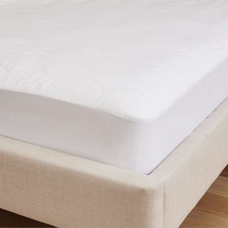 The corner of a white quilted mattress protector on a mattress