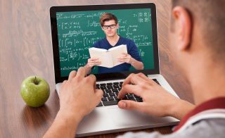 Man works on math problem on laptop computer; monitor features a teacher in front of chalkboard.