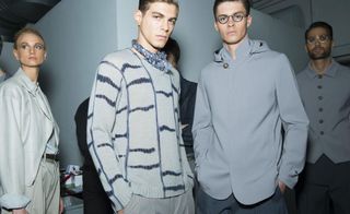 2 male models wearing grey clothing stood in a busy room