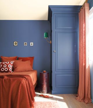 A bedroom painted in a smokey blue shade and with terracotta colored sheets on the bed