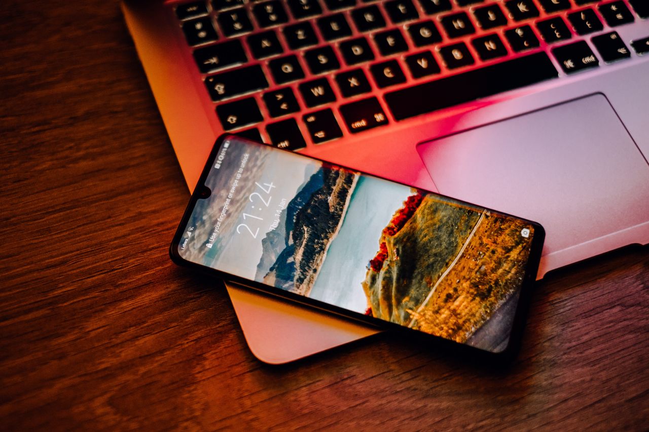 A refurbished Android smartphone sitting on the corner of a refurbished macbook