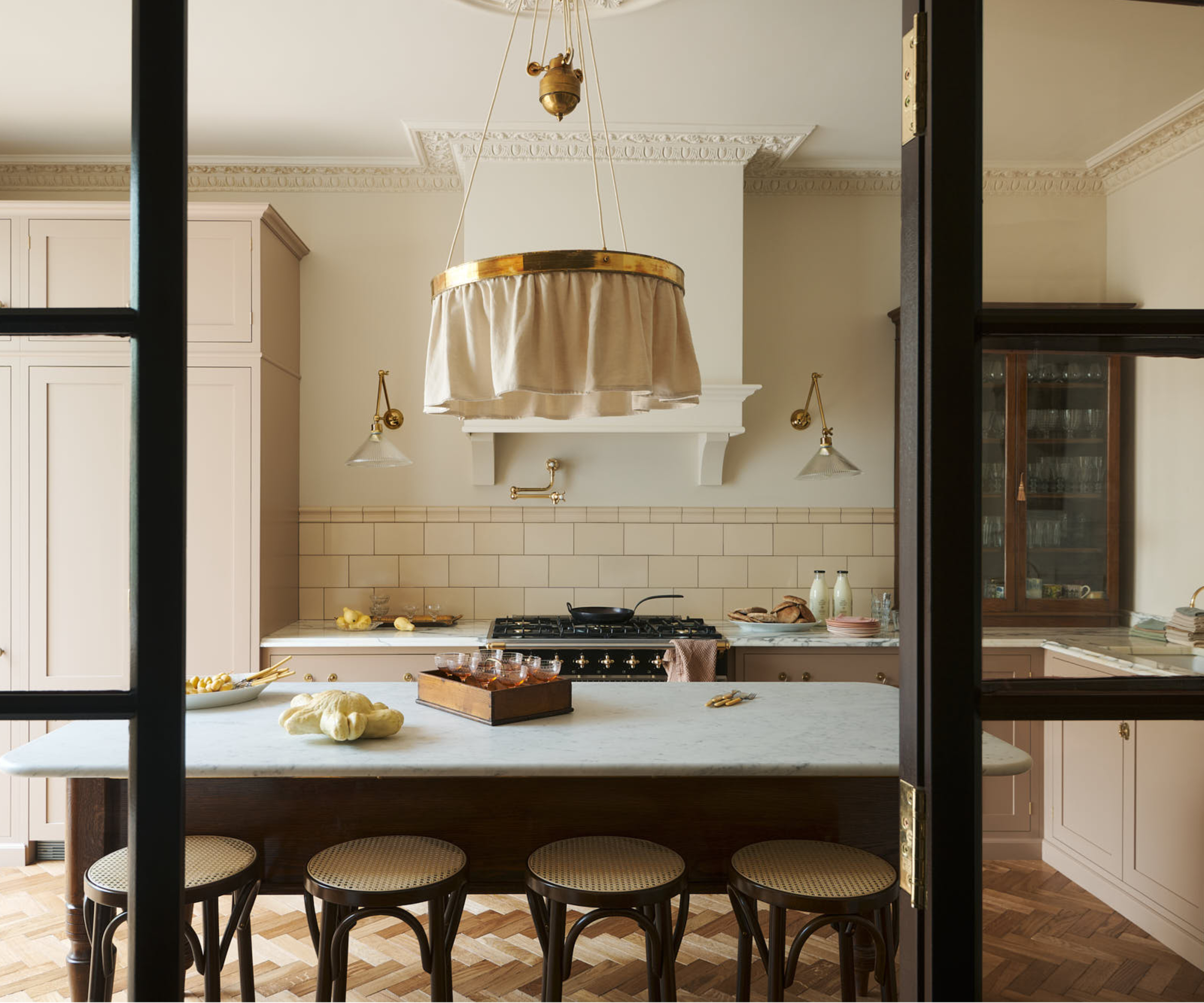 kitchen with large island, decorative fabric and metal large light above island and brass and glass extendable wall lights above cooking and prep area