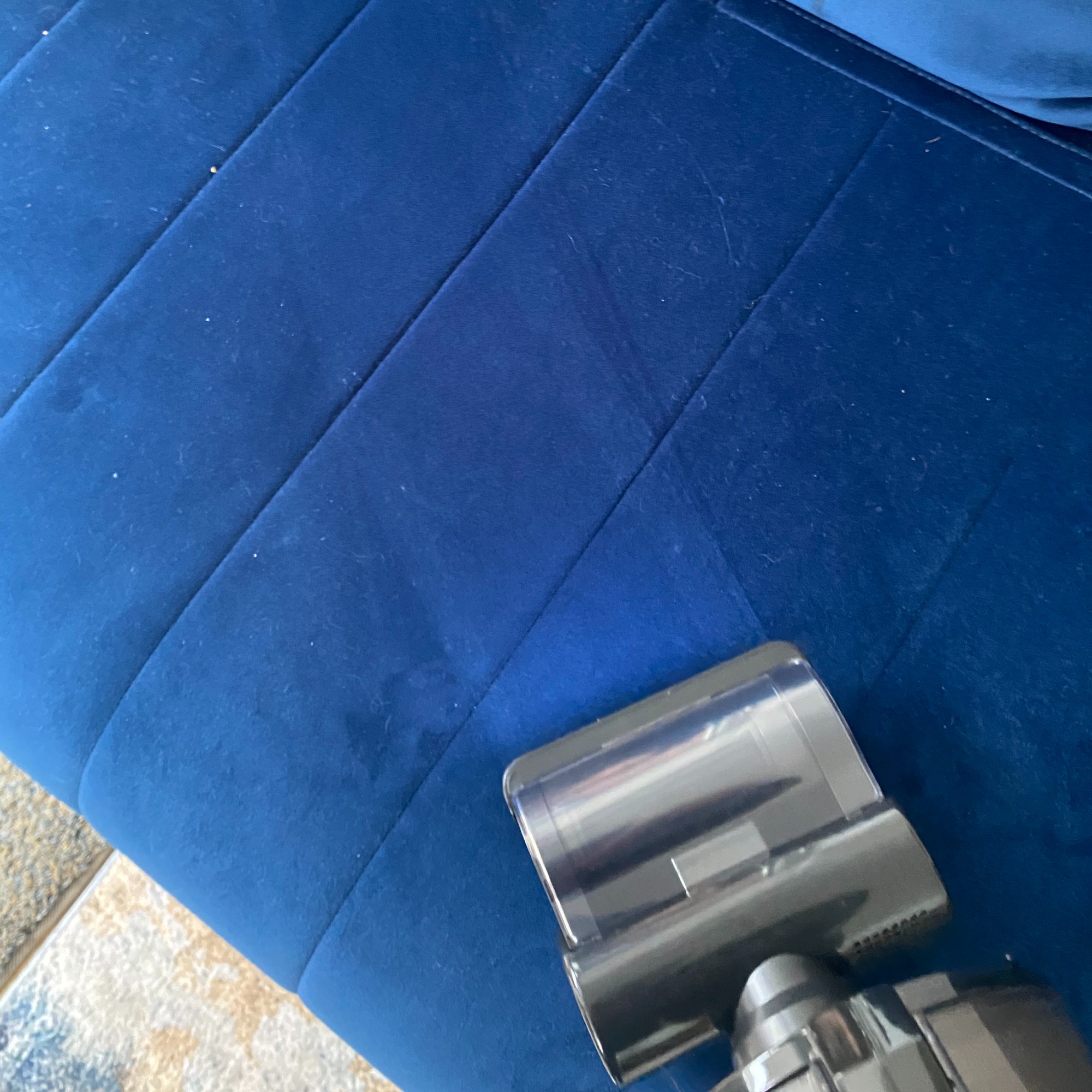 Motorised pet tool attachment of the Hoover HF6 Turbo Sense Pet cordless vacuum cleaner being used to pick up pet hair and debris on velvet sofa bed