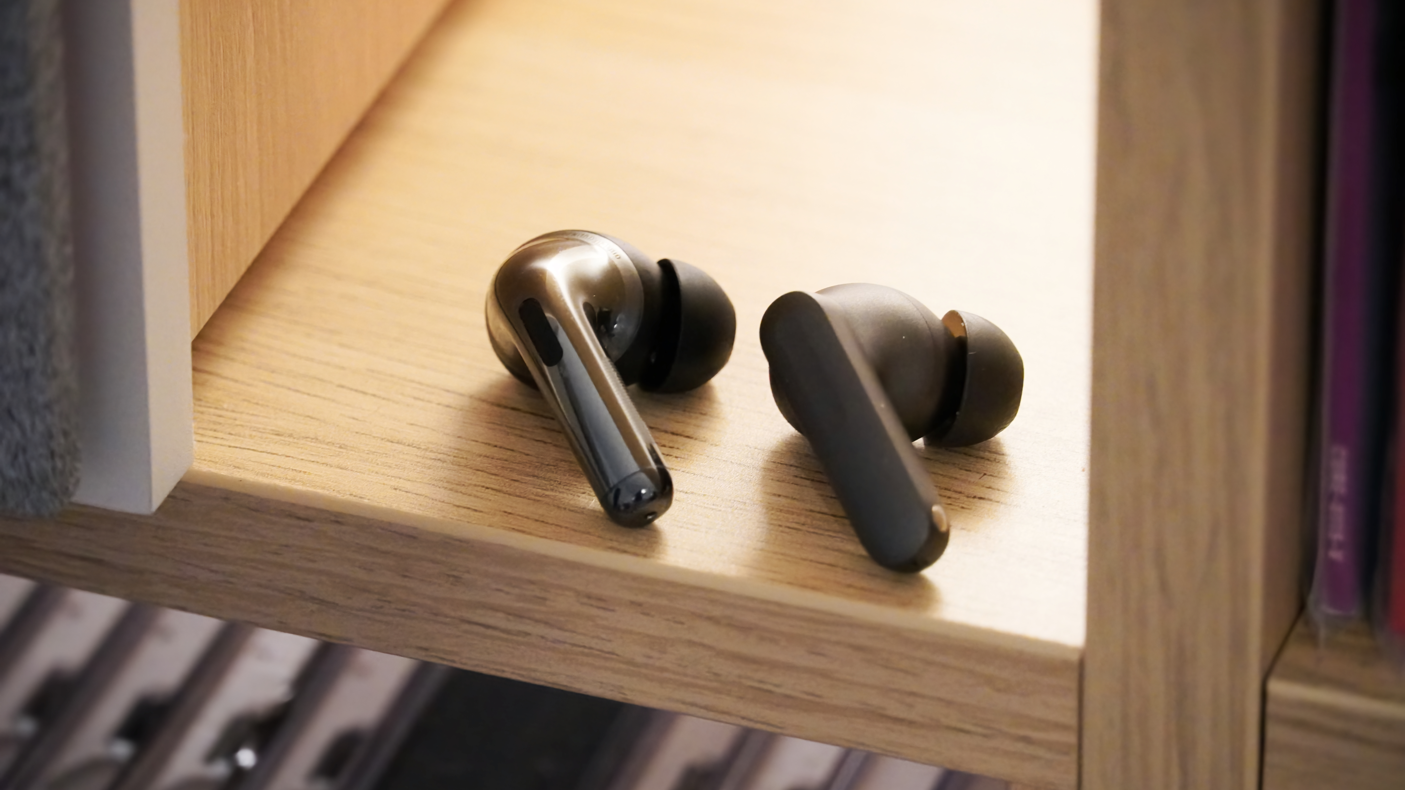 The OnePlus Buds 4 and the OnePlus Buds Pro 3 left earbuds on a shelf.