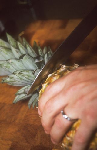 hand and knife slicing a pineapple