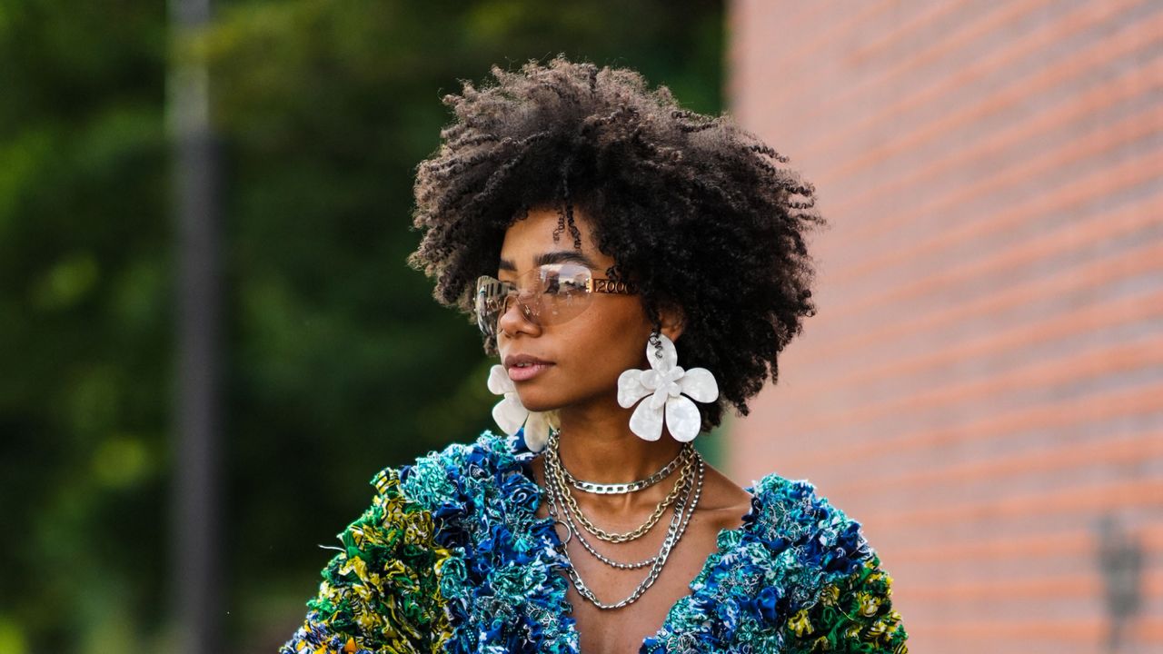 Sarah Monteil wears brown sunglasses, white oversized flower mother of pearl earrings, silver and gold long necklaces, a multicolored / rainbow ruffled oversized long sleeves / short dress, an orange shiny leather handbag, silver rings, white socks from Nike, a white with royal blue shiny leather sneakers from Jordan , outside Alexandre Vauthier, during Paris Fashion Week - Haute Couture Fall Winter 2022 2023, on July 05, 2022 in Paris, France.