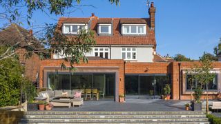 detached house with a large brick-built rear extension and two sets of modern sliding glass doors leading out to a paved patio