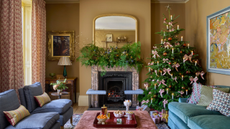 a living room with a teal couch, two blue accent chairs and a coffee table decorated for Christmas with a Christmas tree in one corner and garland on the mantel