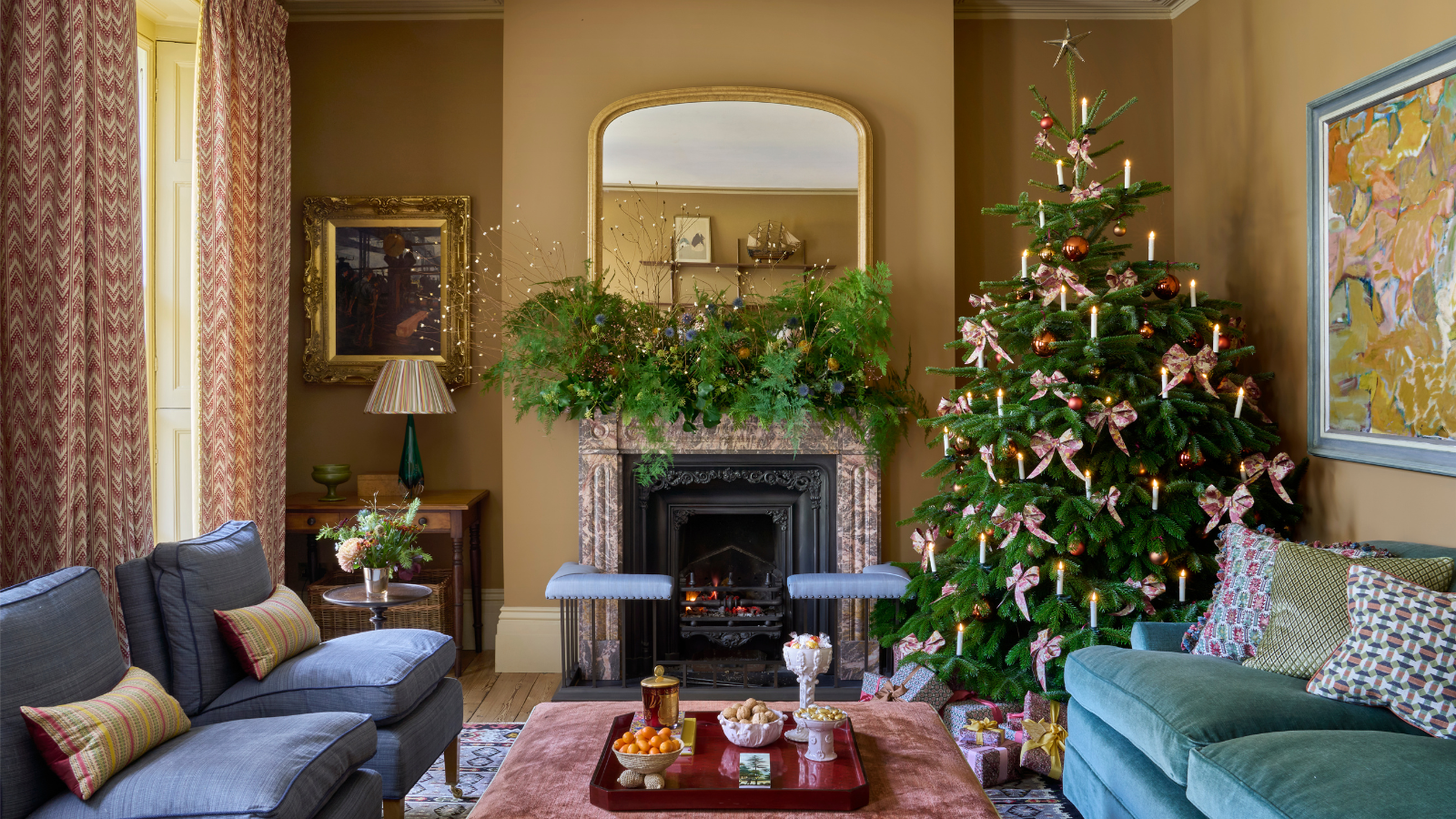 a living room with a teal couch, two blue accent chairs and a coffee table decorated for Christmas with a Christmas tree in one corner and garland on the mantel