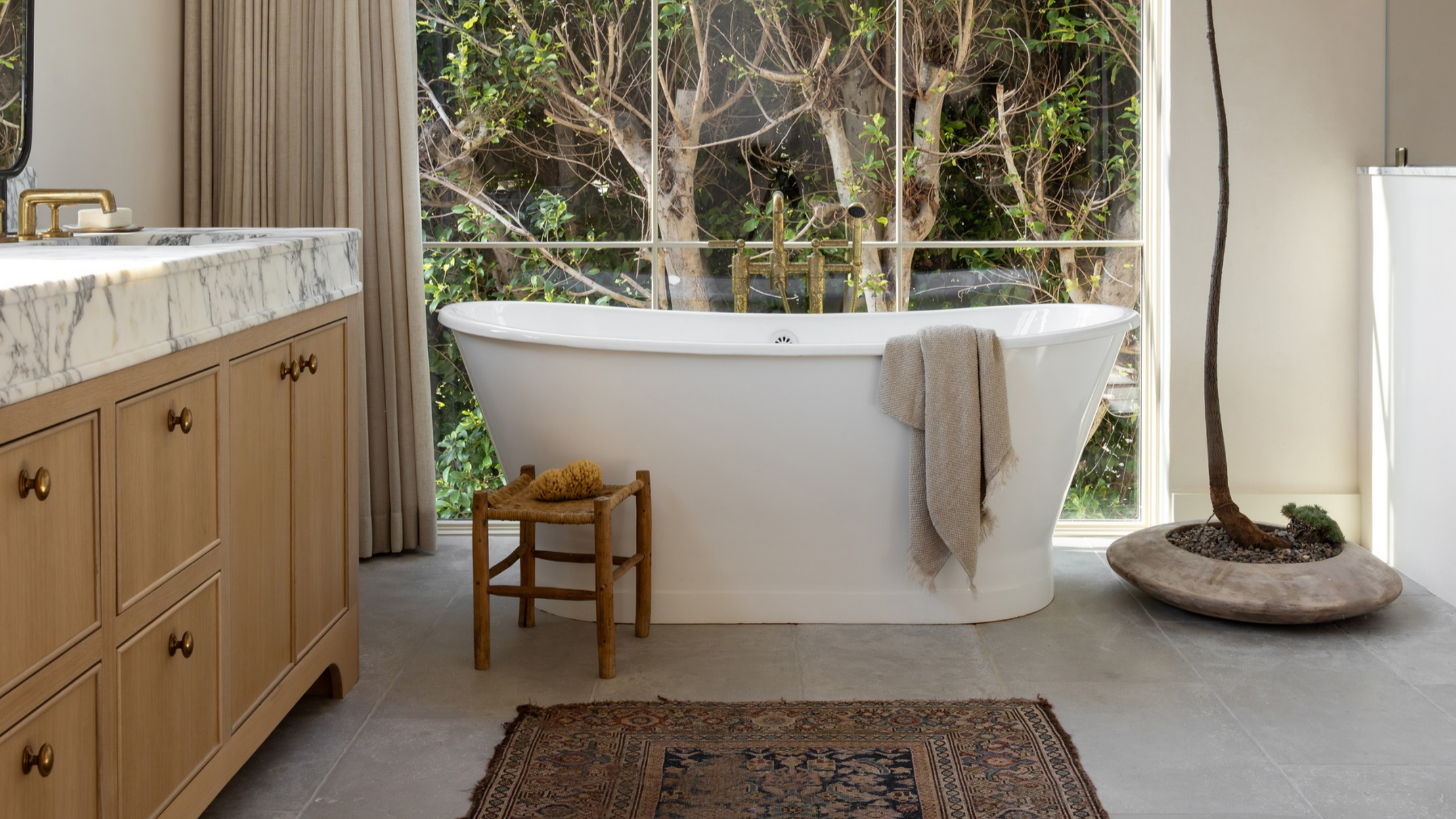 Image of a bathroom with large freestanding bath, wooden cabinetry, a rug and wooden accessories 
