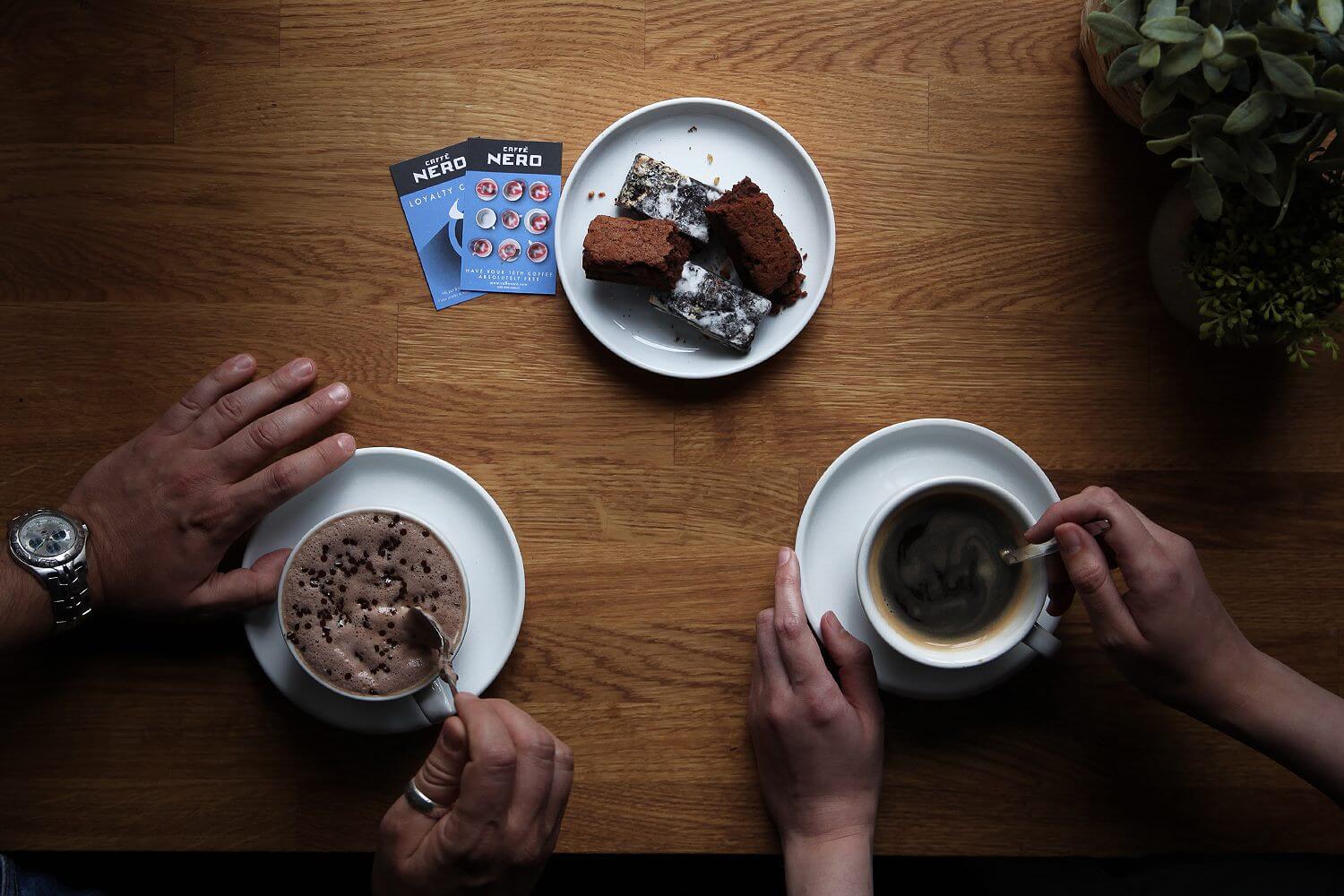 Two Caff&amp;eacute; Nero loyalty cards on a table next to two people having coffee and cake