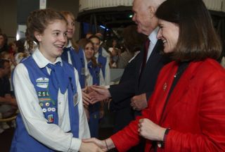 sally ride in a red shirt shaking hands with a girl scout that has badges on her vest