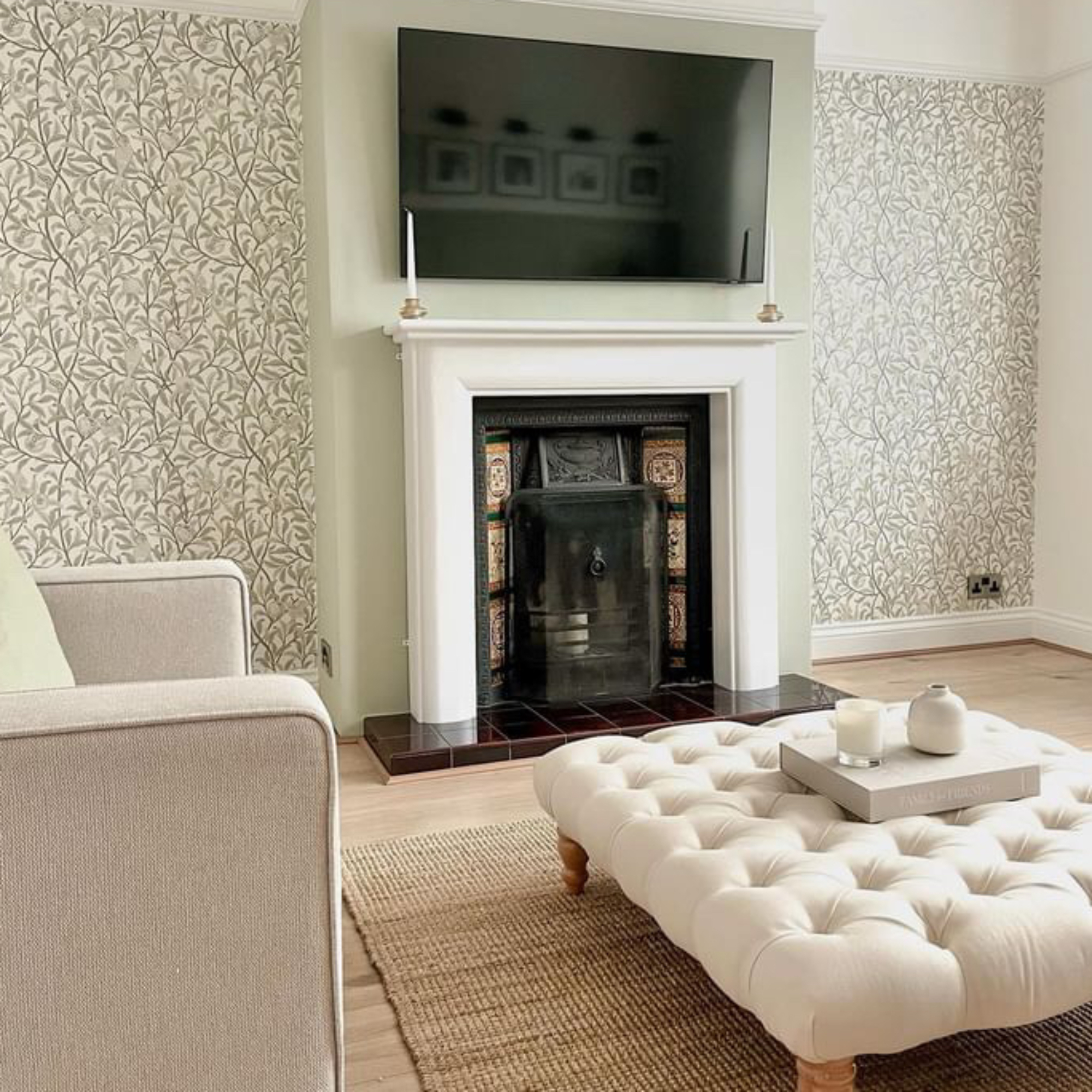 living room with white footstool and fireplace with tv above