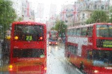 Buses on Oxford Street with Union Jack flags viewed through window with raindrops.