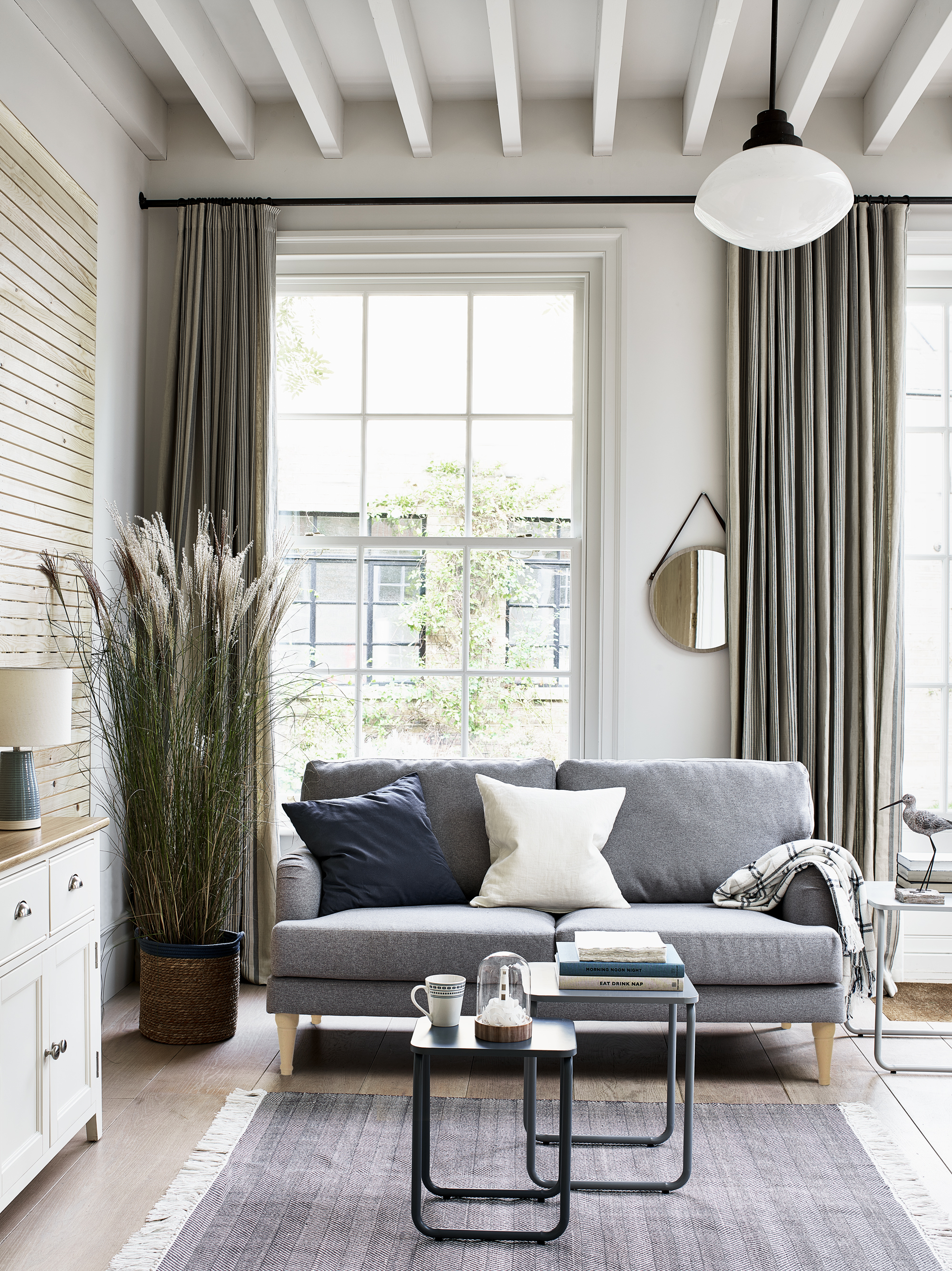 A living room with grey sofa, white beams on ceiling and sage-colored curtains by Argos