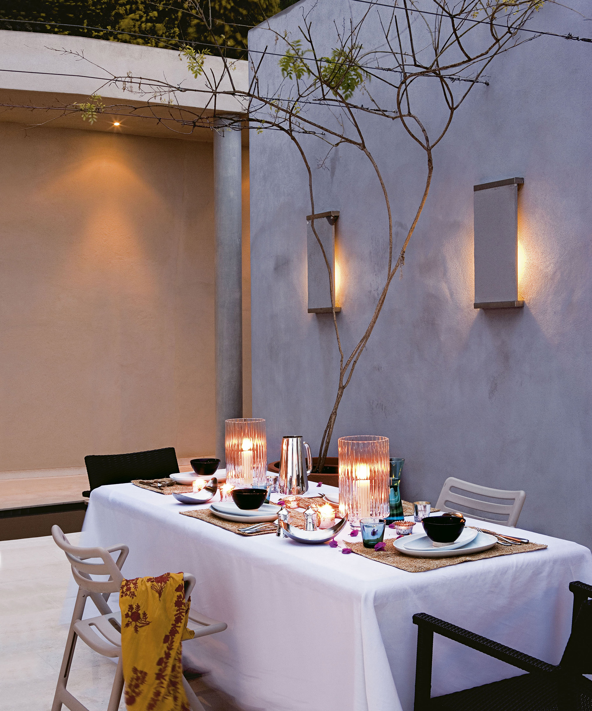 A garden seating area with ambient wall lights and candles lit on the dining table