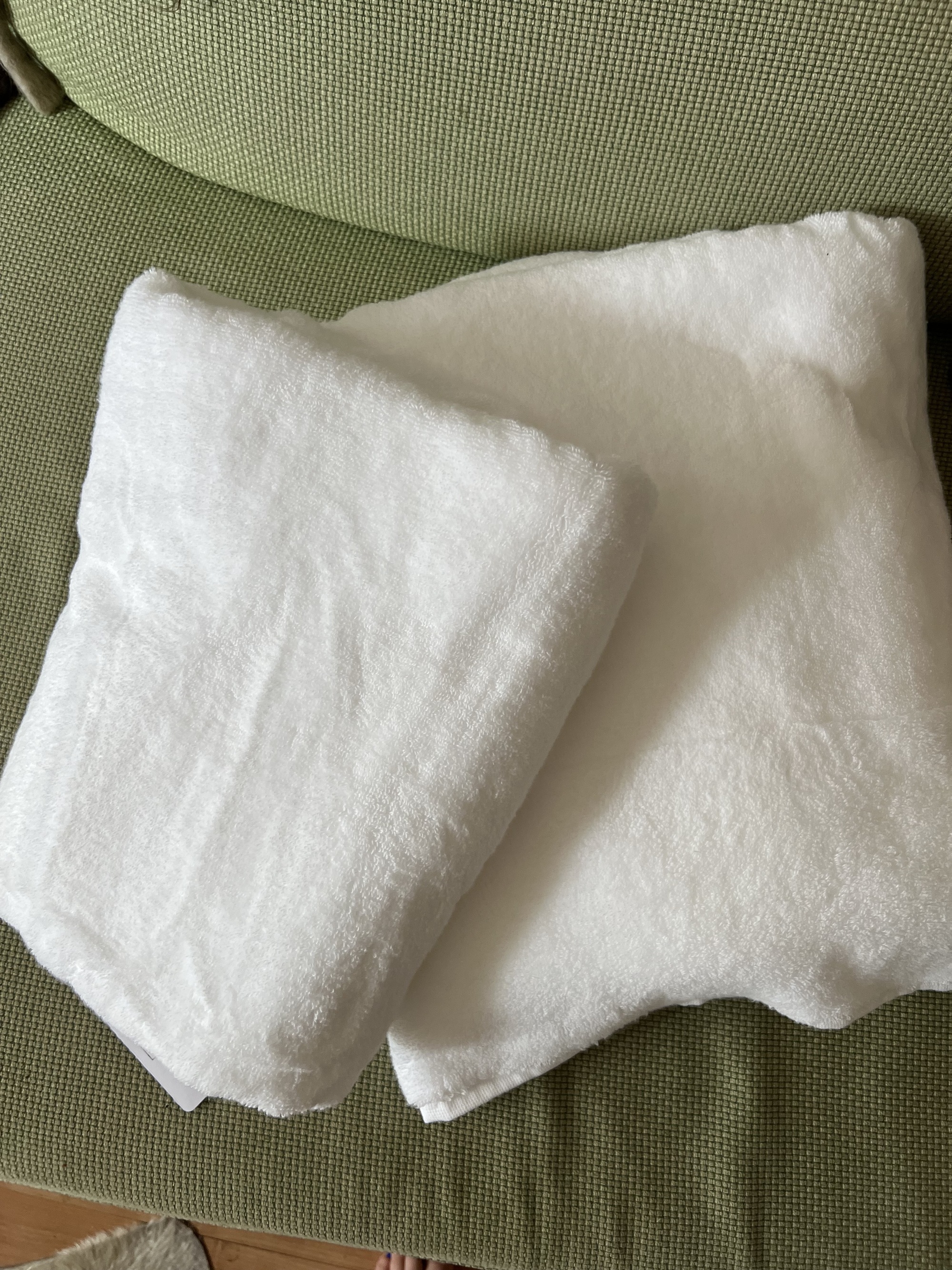 Image of two white towels folded on top of each other on a green sofa.