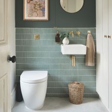 Green bathroom with green tiles above a wall-mounted toilet and sink, with gold fixtures