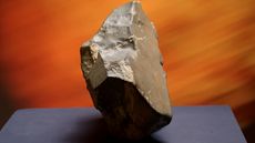 A photo of a large meteorite on a pedestal with an orange background