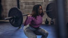 Woman lifting barbell with plate on each end, looking focused at the gym, to represent how long should you lift weights for