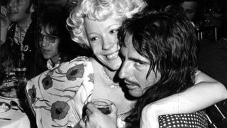 Pamela Des Barres sitting on Alice Cooper's lap in a nightclub 