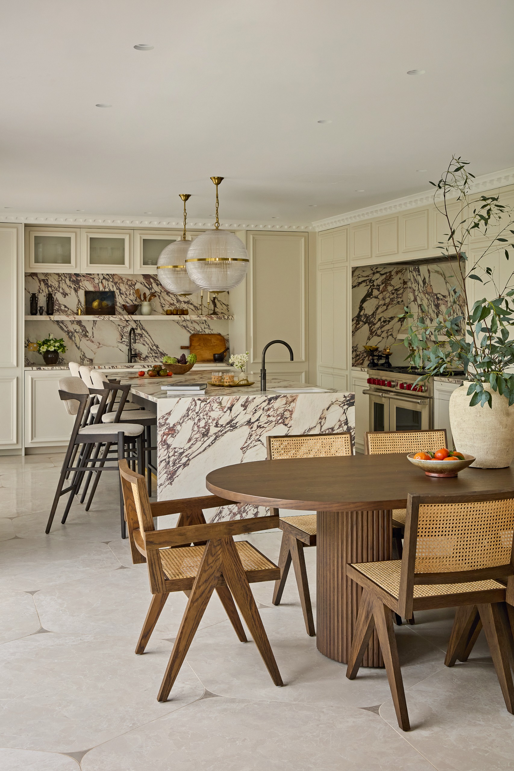 Cream kitchen with black and cream marble countertop, dark wood oval dining table, dark wood and cane chairs and pale grey tiles