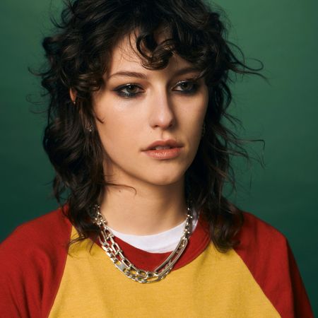 king princess poses with heavy eye makeup and wearing a yellow and red top with a chain necklace