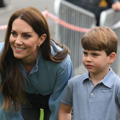 Princess Kate wears a blue shirt and stands with son Prince Louis, who is wearing a blue and white checked shirt