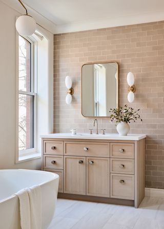 A bathroom in muted tones, with white and brass sconces installed next to the mirror
