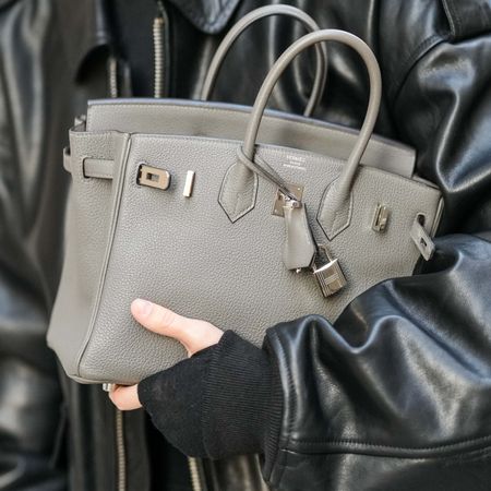 a Birkin Bag with light damage in someone's arms at fashion week with a leather jacket