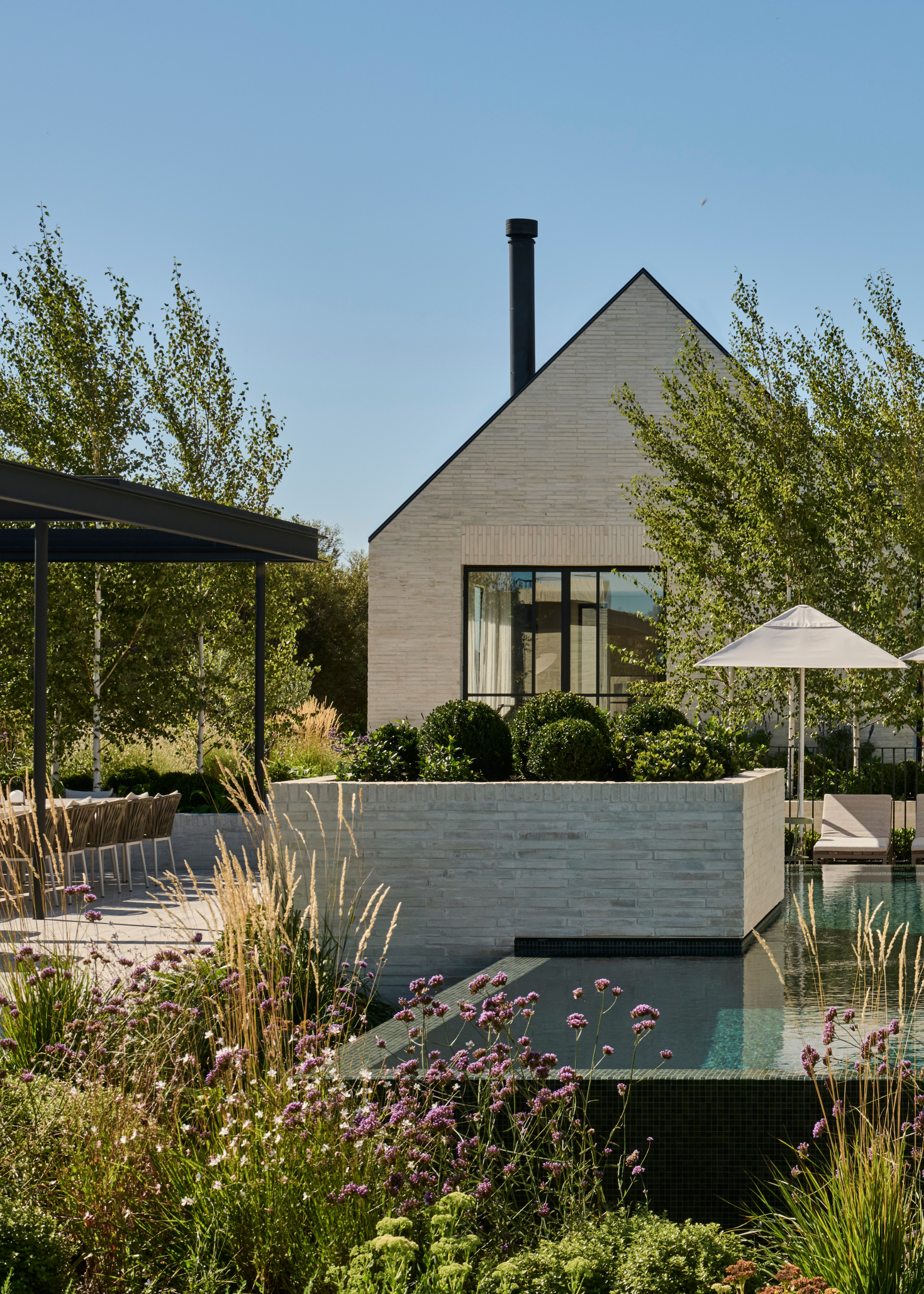 An outdoor garden with a pool, flowering patches, and round topiarised bushes
