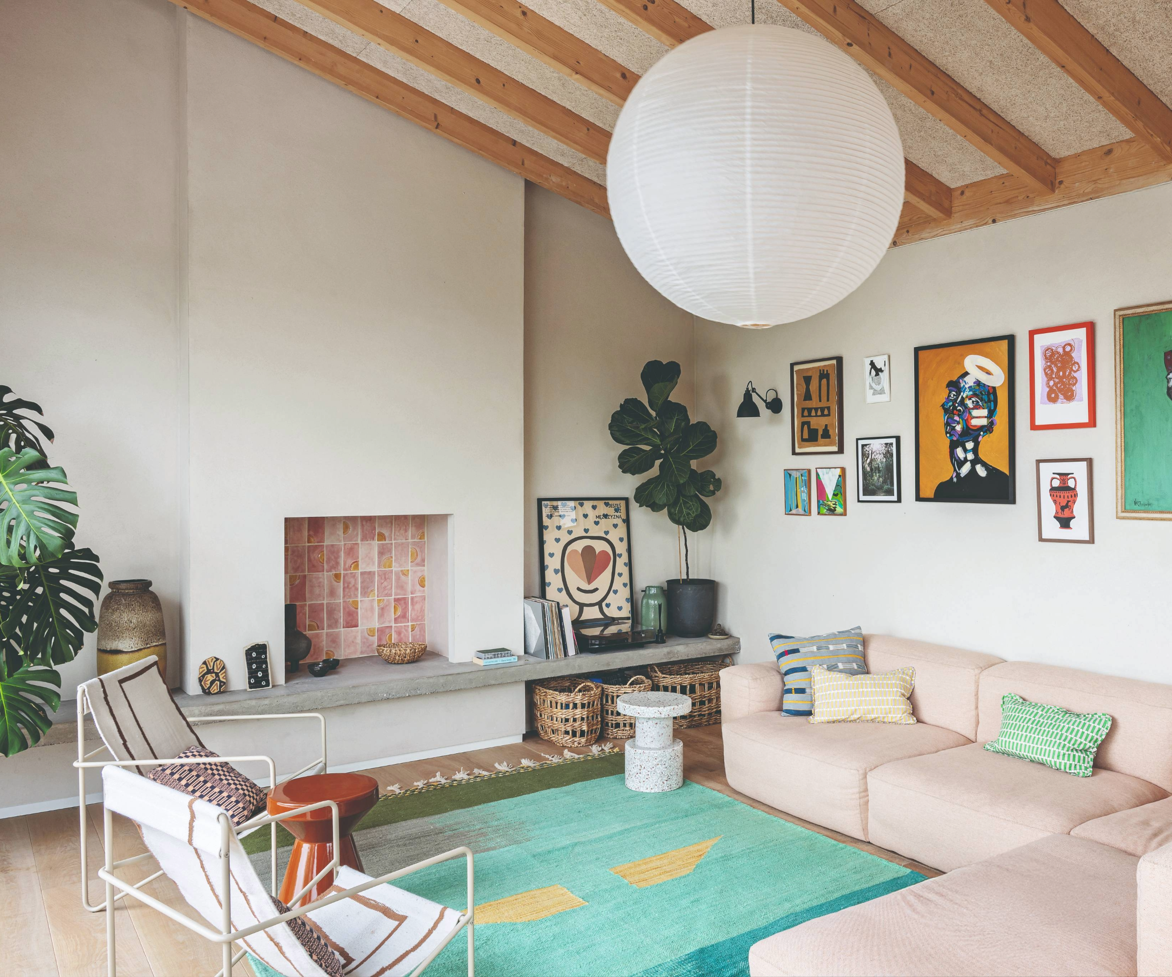 Living room with a pastel pink L shaped sofa, colourful art, pink tiled fireplace, and blue rug