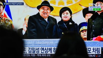 People watch a television screen showing Kim Jong Un and his daughter attending a military parade