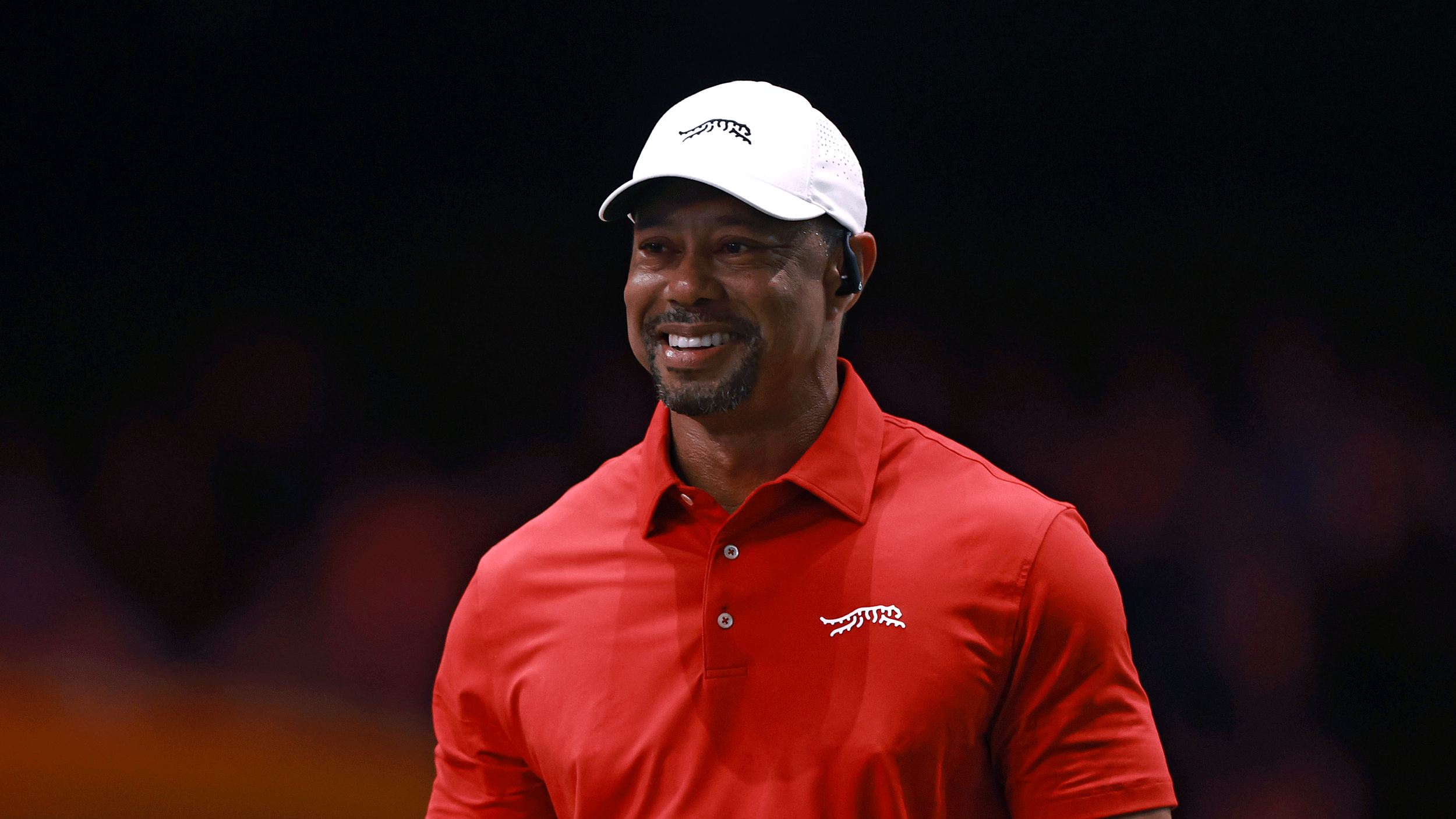 Tiger Woods smiles while wearing a white Sun Day Red cap and a red Sun Day Red polo during a TGL match in 2025